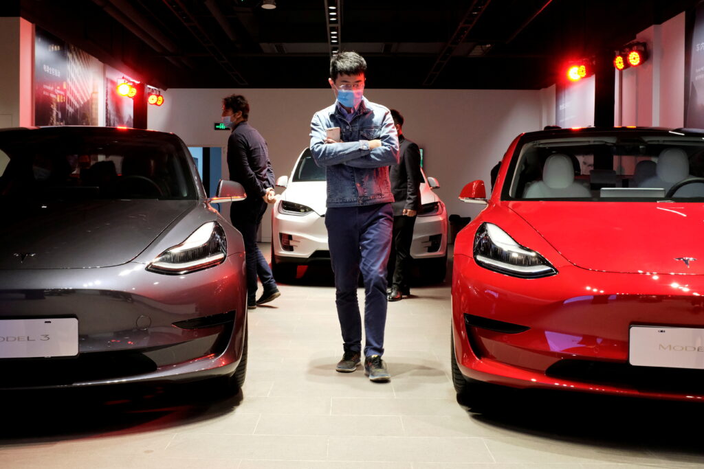 FILE PHOTO: Man walks by Tesla Model 3 sedans and Tesla Model X sport utility vehicle at a new Tesla showroom in Shanghai